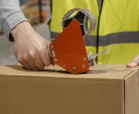 Aplicação de fita adesiva industrial em caixa de papelão em ambiente logístico exigente, com uso de aplicador manual.