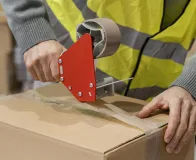 Aplicação de fita dupla face industrial em caixa de papelão para fixação e fechamento em ambiente logístico.