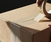 Aplicação de fita adesiva para embalagem em caixa de papelão, garantindo vedação segura para transporte.