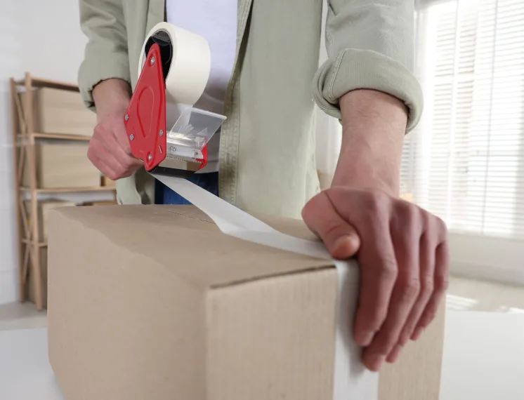 Aplicação de fita adesiva para embalagem em caixa de papelão com aplicador manual.